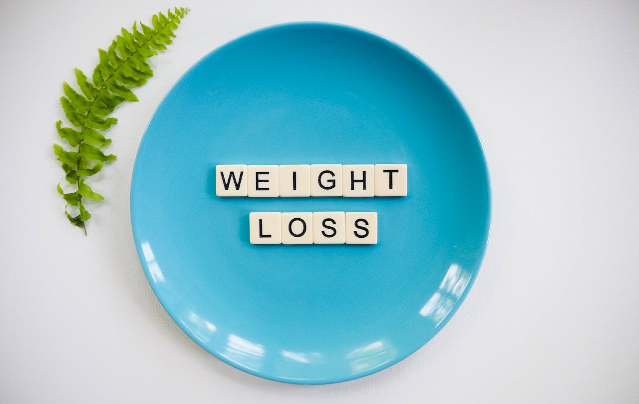 hero-img-01 A blue plate with 'weight loss' tiles and a fern leaf on white background.
